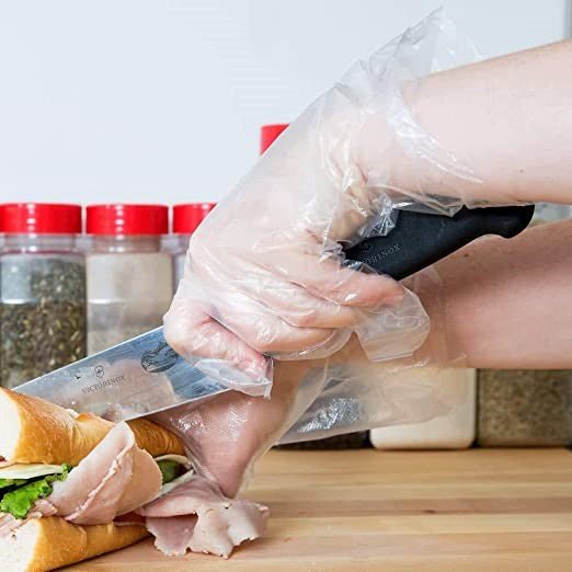 Individual wearing diamond clear polyethylene gloves while slicing a sandwich