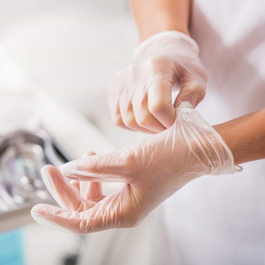 An individual in a white coat donning Diamond Clear Vinyl Exam Gloves