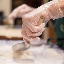 A person preparing dough on a table while wearing Diamond Clear Vinyl Exam Gloves